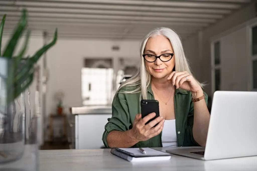 A smiling woman holds up a smartphone to look at screen.
